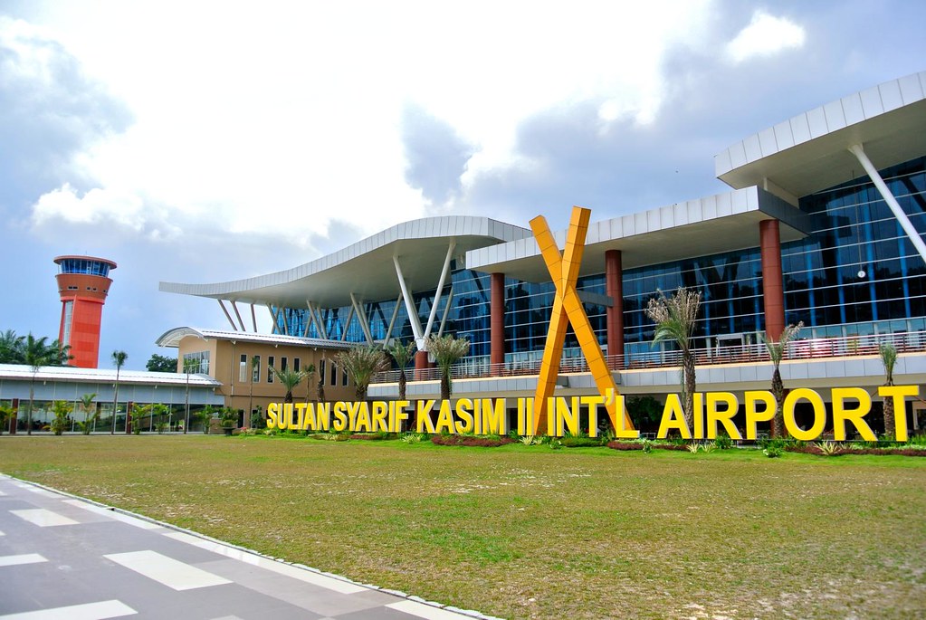 Bangunan Bandara Sultan Syarif Kasim II terlihat modern dengan dinding-dinding kaca. Terlihat tulisan nama bandara berwarna kuning.